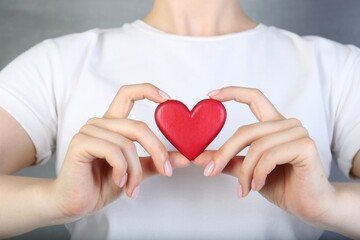 Woman holding red heart on grey background, closeup