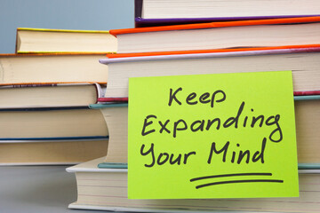 Stack of books and a note with the phrase Keep expanding your mind. Continuous learning and personal growth.