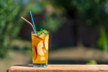 One glass of a summer cocktail or cold tea with peach slices, ice and mint on the nature...