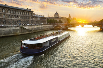 The Seine River in Paris with a historic bridge and the illuminated Eiffel Tower in the background. A cruise boat sails along the river against the backdrop of an evening sunset. Very romantic