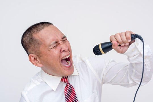 A middle aged asian man in office attire singing loud and unpleasantly, with a grating tone-deaf voice. Improper singing technique during karaoke time. Isolated on a white background.