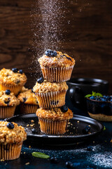 Blueberry muffins placed one on top of the other are sprinkled with powdered sugar on top