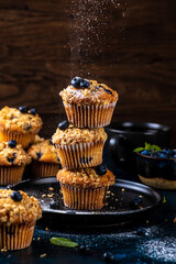Blueberry muffins placed one on top of the other are sprinkled with powdered sugar on top