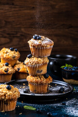 Blueberry muffins placed one on top of the other are sprinkled with powdered sugar on top