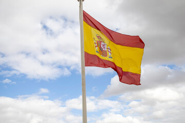 The bright sun illuminates the red and yellow stripes of the flag, creating a vibrant contrast against the backdrop of the blue sky and fluffy clouds. This image personifies the strength and beauty of
