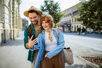 Young couple, on a vacation, exploring the new city and using their phone as gps to help them not...