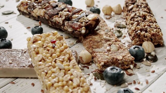 Close-up of assorted healthy granola bars with fresh blueberries and various nuts on a wooden table. Ideal for promoting nutritious snacks and a healthy lifestyle.