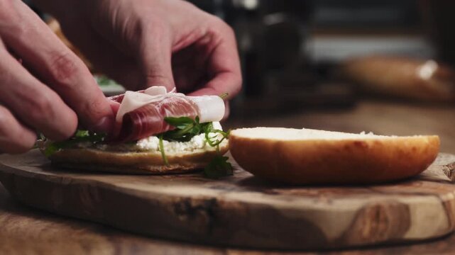 Man hands put prosciutto on bagel on wood board