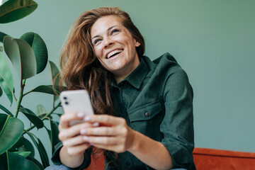 Cheerful happy freckled woman reading a chat message on her mobile phone.