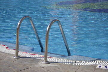 Detalle del borde de piscina y escalera con el agua refrescante azul en referencia al verano