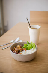 Ricebowl Beef Barbeque in a white bowl on a natural wood color table with ice tea on white paper cup