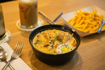 Thick curry noodles in a bowl, large portions of french fries, palm sugar milk coffee, mocha latte coffee served together on the cafe table