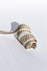Color vertical photo, white fabric ribbon with a brown pattern, twisted in a spiral, the object is used in sewing firefighting overalls and uniforms, with a white background.
