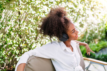 black teenage listening music wearing headset. young female student enjoying calm song sitting chilling outside. african american student enjoying listening music using wireless headphones on head