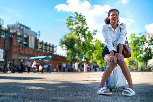 lost black girl tired sitting baggage on vacation. exhausted young teenage tourist sitting on luggage at gateway brick wall landmark. fatigued african american girl confused lost location destination