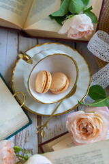 Roses, a porcelain cup and saucer and small cakes on a table with books.
