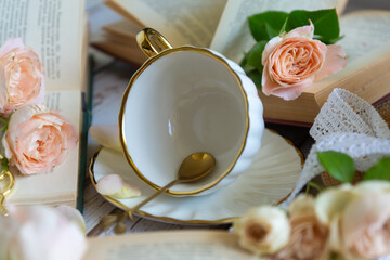 Roses, a porcelain cup and saucer and small cakes on a table with books.
