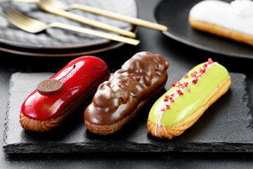 Set of beautiful french eclairs with different colorful toppings on black background