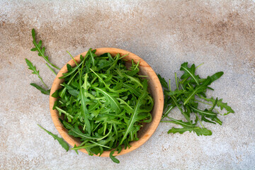 Fresh arugula leaves in wooden bowl on concrete background. Top view.