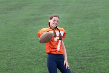 A smiling girl or young woman in a sports uniform is holding a ball in front of her, looking at...