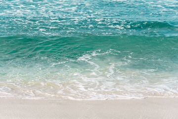 Blue ocean waves cover the sand on the beach in summer