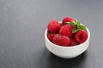 ripe raspberries in white bowl on slate background