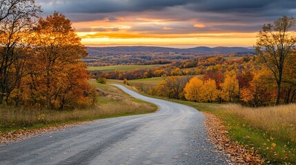 Fototapeta premium An autumn landscape featuring a long, winding road lined with trees in full fall color, with a thick carpet of leaves covering the road and the distant hills bathed in the golden light of sunset