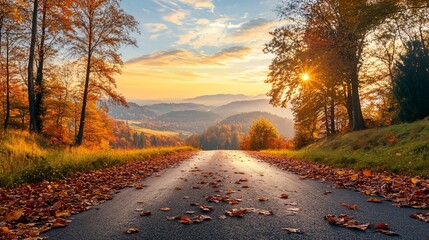 Obraz premium An autumn landscape featuring a long, winding road lined with trees in full fall color, with a thick carpet of leaves covering the road and the distant hills bathed in the golden light of sunset