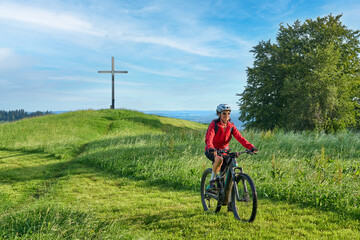 Fototapeta premium pretty senior woman riding her electric mountain bike and enjoying the spectacular view over the Allgau alps below the Nagelfluh mountain chain next to Steibis, Bavaria, Germany 