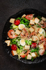 caesar salad with tiger prawns, shrimp salad, lettuce leaves, quail eggs, cherry tomatoes, parmesan cheese, on a black plate,