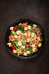 caesar salad with tiger prawns, shrimp salad, lettuce leaves, quail eggs, cherry tomatoes, parmesan cheese, on a black plate,
