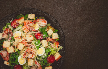 caesar salad with tiger prawns, shrimp salad, lettuce leaves, quail eggs, cherry tomatoes, parmesan cheese, on a black plate,