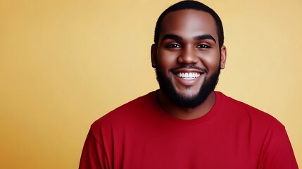 Obraz premium A smiling African American man in a red shirt poses against a bright yellow background, exuding warmth and positivity, showcasing his well-groomed beard and joyful demeanor.