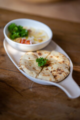 Traditional Naan bread with hummus and garnish on a wooden table, great as appetizer or snack