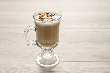 Cappuccino coffee in a glass cup on a white wooden table.