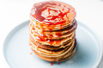 Pancakes stacked on a turquoise plate on a white background with sea buckthorn and tea.