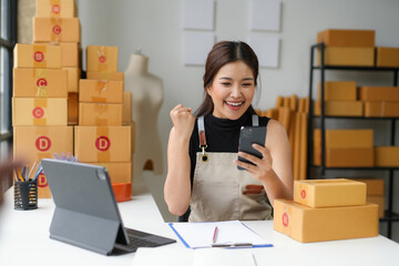 Asian sme business woman using smartphone checking customer order online and preparing to packing...