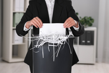 Woman destroying sheet of paper with shredder in office, closeup