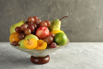 Glass vase with different fresh fruits on gray textured table, space for text