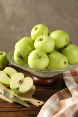 Glass vase with fresh green apples, cutting board and knife on wooden table against gray background, closeup