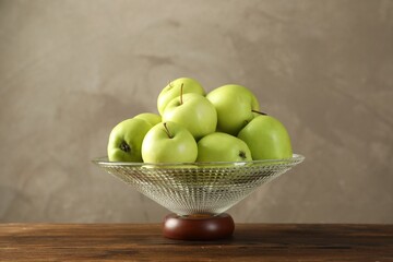 Glass vase with fresh green apples on wooden table against gray background