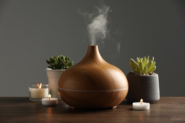 Aroma oil diffuser, houseplants and burning candles on wooden table