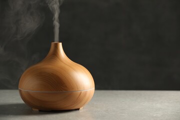 Aroma oil diffuser with steam on light grey table, space for text