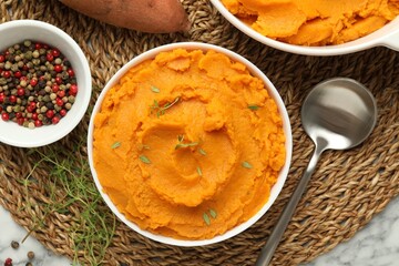 Delicious mashed sweet potatoes in bowl, spoon, microgreens, spices and vegetable on white marble table, top view
