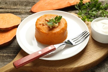 Tasty mashed sweet potato, parsley and walnuts served with sauce on wooden table, closeup