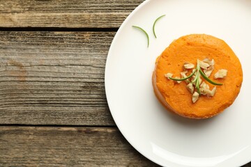 Plate with tasty mashed sweet potato, rosemary and walnuts on wooden table, top view. Space for text