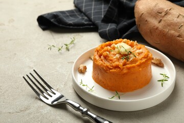 Plate with tasty mashed sweet potato, butter, thyme and walnuts on grey textured table, closeup