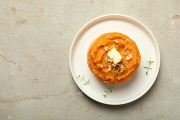 Plate with tasty mashed sweet potato, butter, thyme and walnuts on grey textured table, top view. Space for text