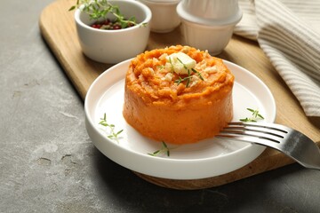 Plate with tasty mashed sweet potato, butter, thyme and walnuts served on grey textured table, closeup
