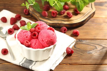 Delicious raspberry sorbet with fresh berries in bowl and spoon on wooden table